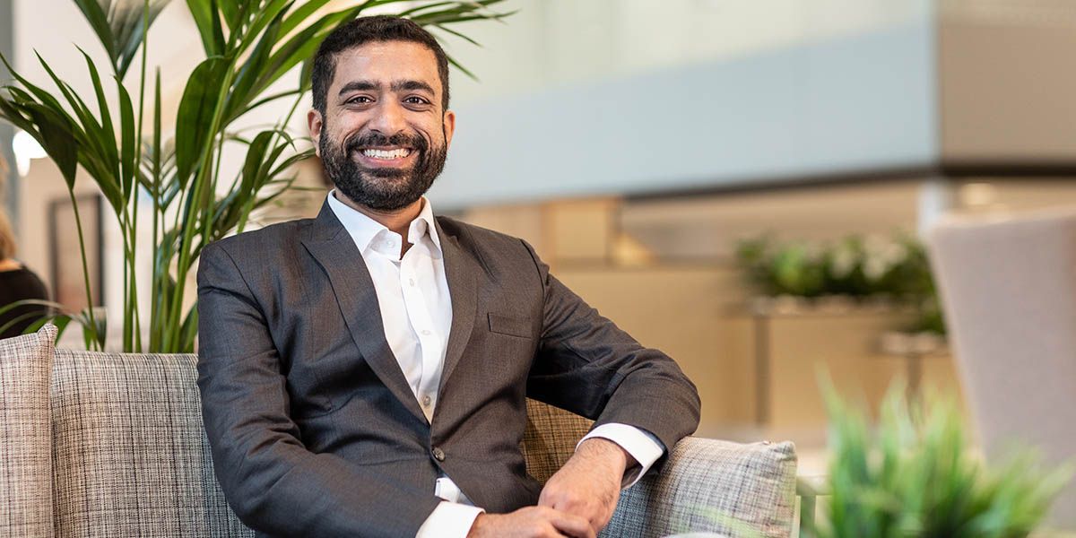A student in a suit, smiling to camera in a cafe environment.
