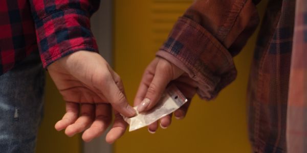 A student's hand passing a bag of white powder into another student's hand