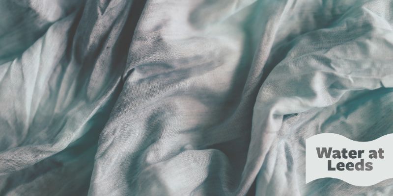 Scrunched up fabric with dark stains on it. The wave-shaped logo in the corner reads Water at Leeds.