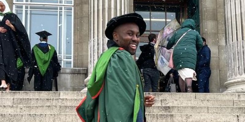 Craig Poku stands on the Parkinson steps in graduation attire