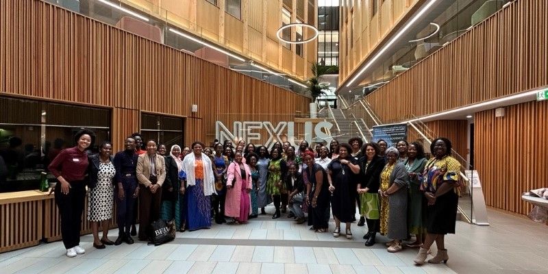 A large group of women from the Black Female Academics Network smiling at the camera in the Nexus foyer.