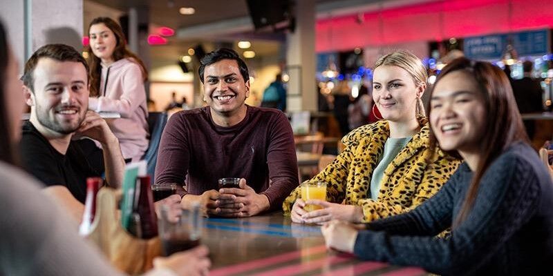 Four international students sit at a table in a café smiling together.