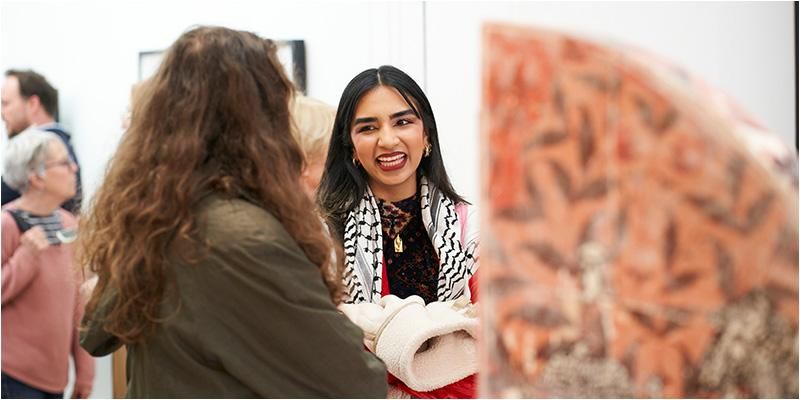 Two people smiling at each other as they look at a piece of art on display at an exhibition.