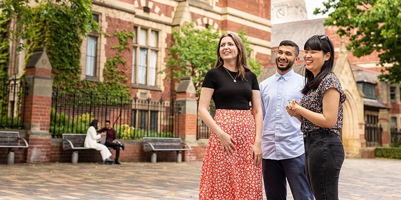 Three students standing on campus with the Great Hall and Parkinson Building tower in the background.