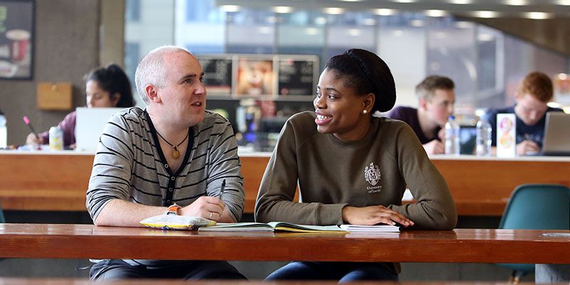 Two students sat smiling at a table in the in the Waterside Cafe.