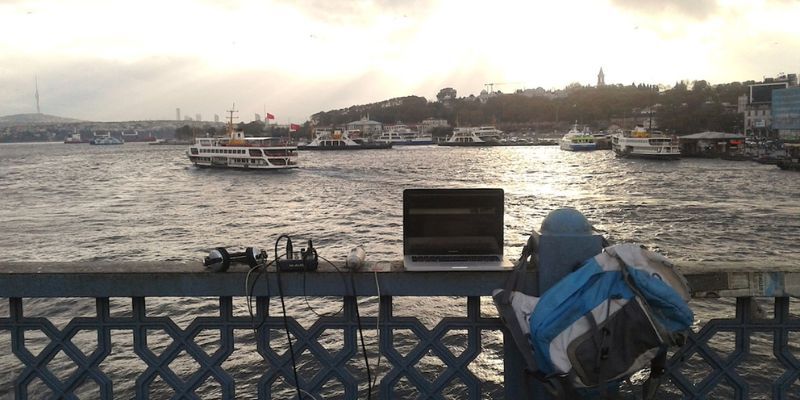 Sound recording session overlooking the Bosporus, Istanbul. A laptop and sound equipment are set up on an intricate bridge overlooking the strait. Several boatsare on the wateer.