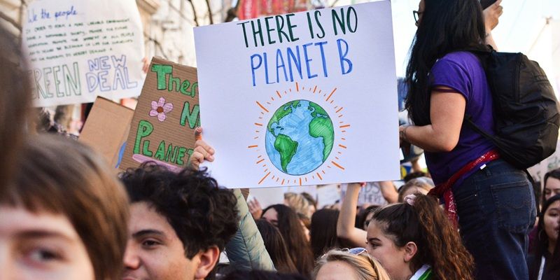 A crowd of people on a march against climate change. Several are holding placards. One says: There is no planet B.