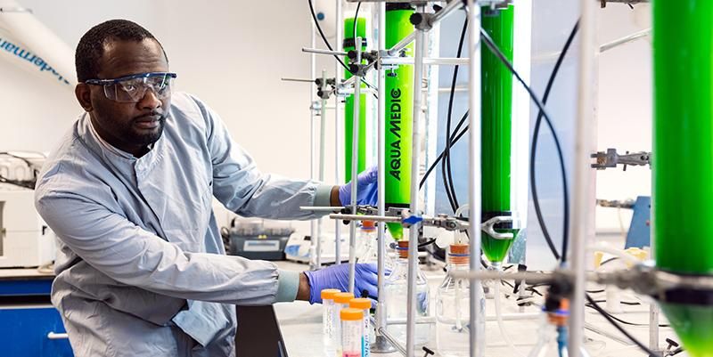 A researcher in a lab coat working with test tubes and machinery in a lab