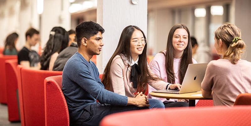 Four people sat around a table, with one person looking at a laptop