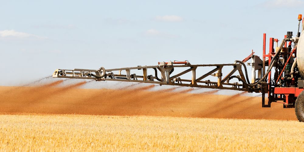An arm extending from a large vehicle spreading sludge onto agricultural land.