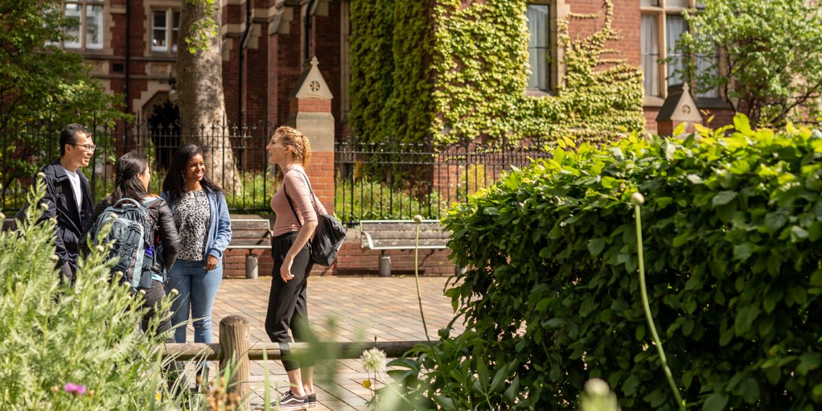Four students stand outside on campus talking to each other.