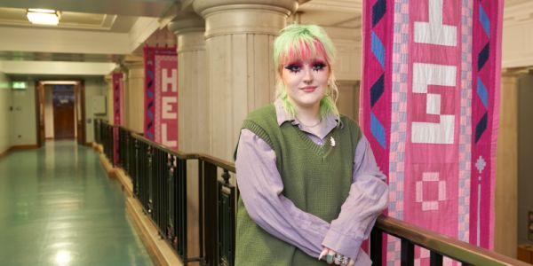 Tiegan Handley stands in Parkinson Court with large banners they designed hanging behind them