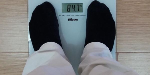 The image shows someone standing on a set of weighing scales. You can only see them from their knees down.