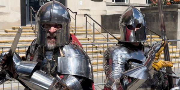 Two people dressed in armour pose for the camera, holding their swords up,