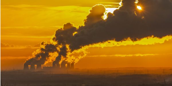Emissions streaming from power station cooling towers at dusk, with a yellow  sky in the background.