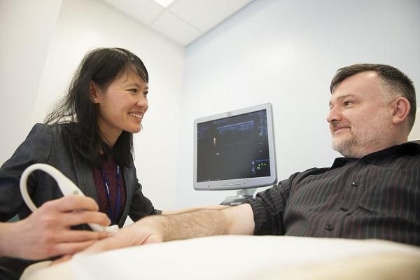 A doctor performing an ultrasound on a patient's hand in a hospital