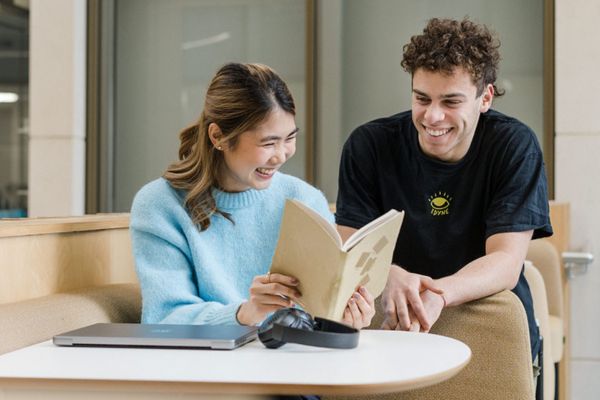 Two students smiling in a study space, using a laptop.
