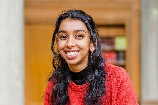 Henna smiling at the camera with a shelf of books in the background