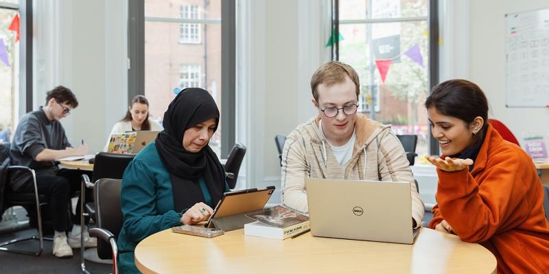 A group of mature students sitting at a table working n laptops and tablets