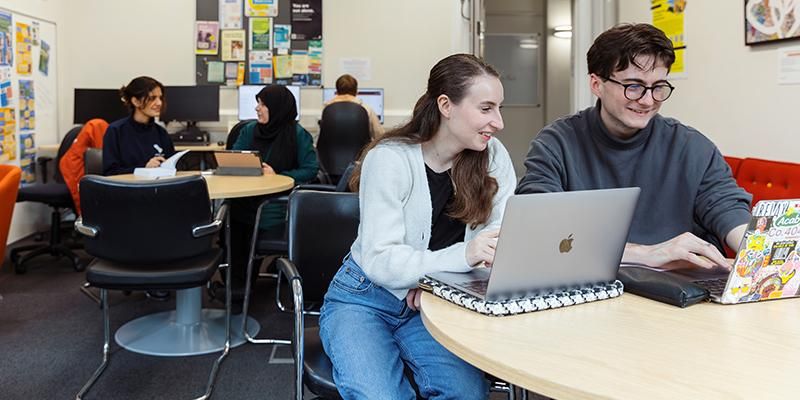 Two mature students working together at a desk with laptops