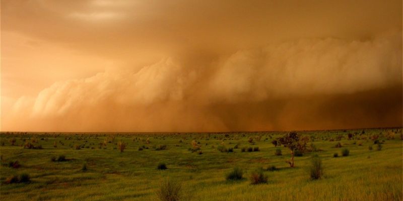 A panoramic picture of a huge storm approaching in a rural African landscape. The impending weather system has turned the sky orange.