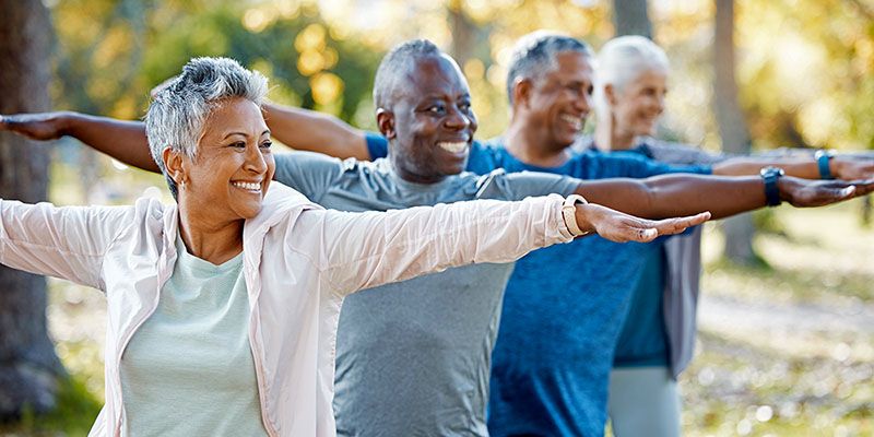 Four older people exercising outside in the sunshine.