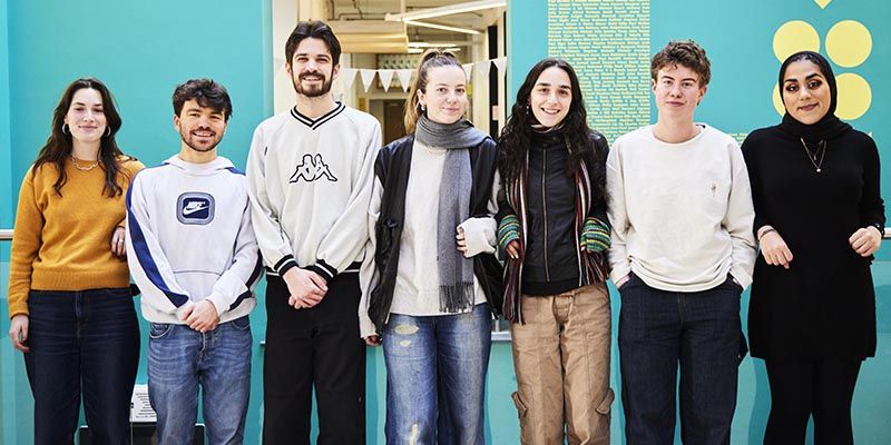 Seven students stood in a line smiling, within the Leeds University Union.