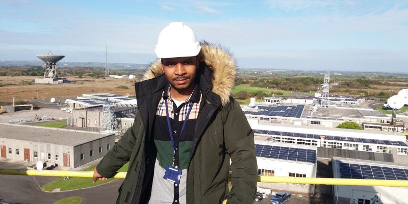 Saul Phiri, wearing a hard hat. Behind him is a series of buildings and satellites.
