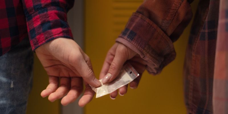 A student's hand passing a bag of white powder into another student's hand