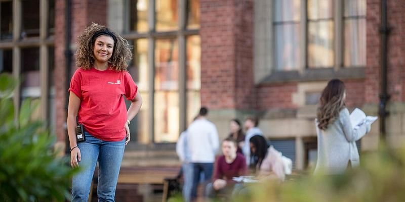 A student ambassador on campus during open day, smiling at the camera. People are looking round in the background.