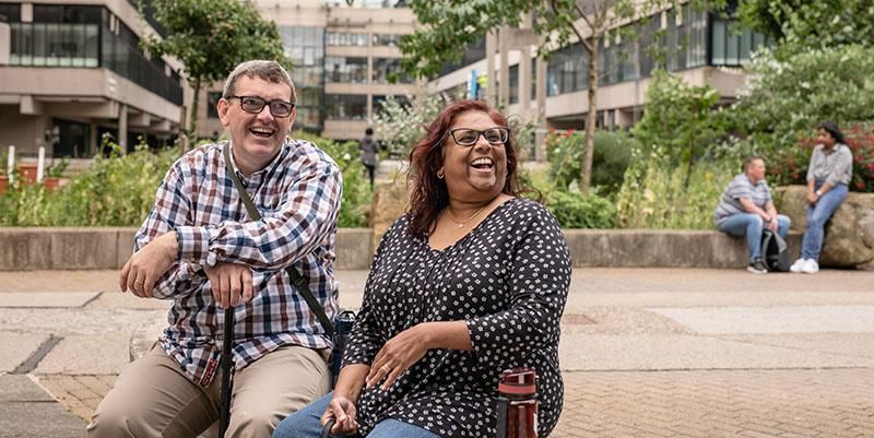 Two mature students sitting on campus laughing