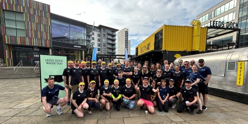 A large group of people by Leeds Dock smiling at the camera.