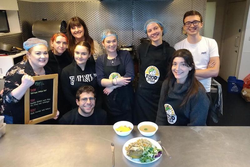 Group shot of students volunteering for FoodCycle. There is a three-course meal on a table before them.