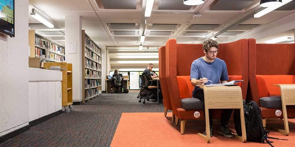 Student working in the library sat in a brightly coloured study booth